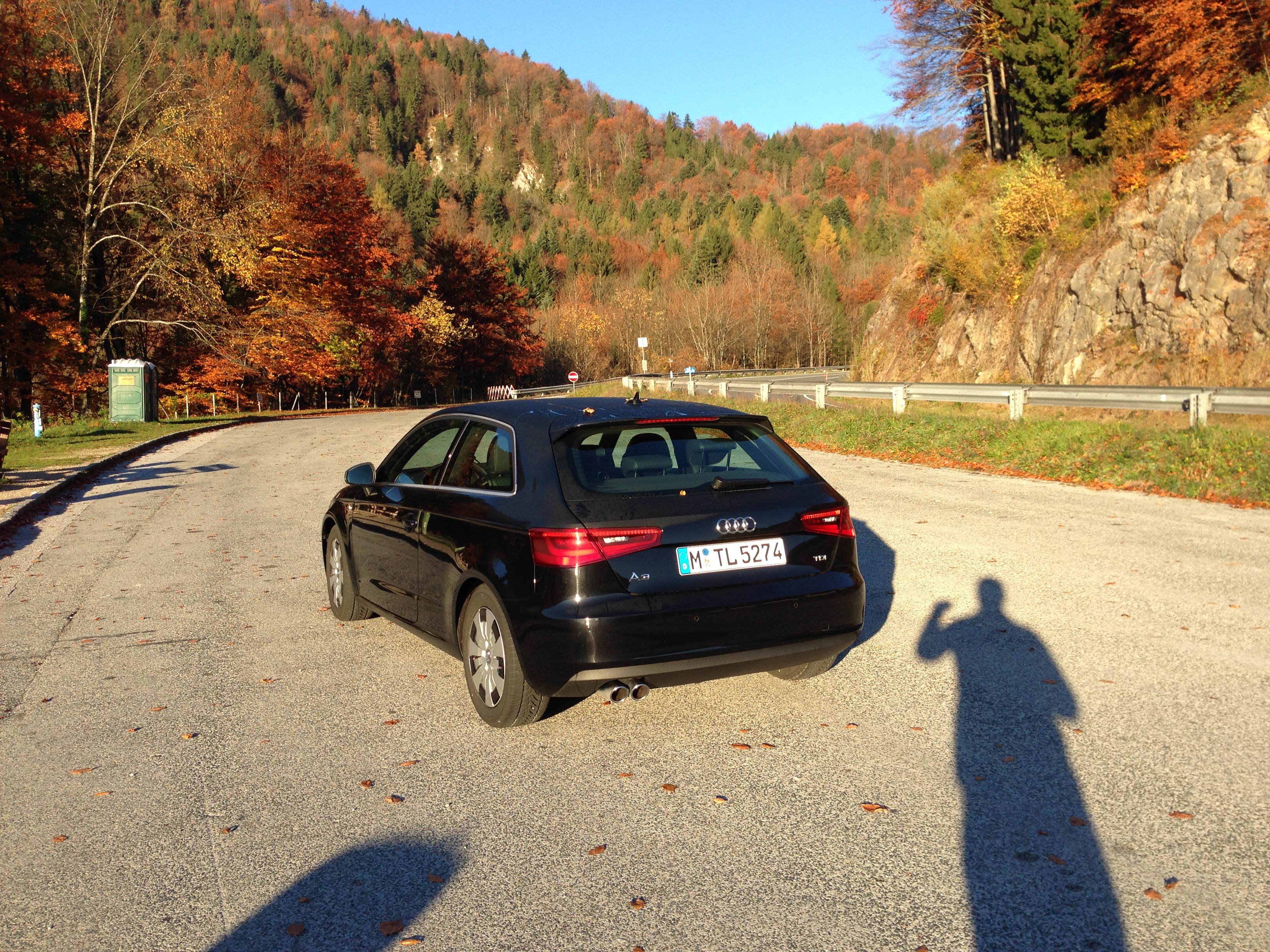 a car parked on a road with a person's shadow