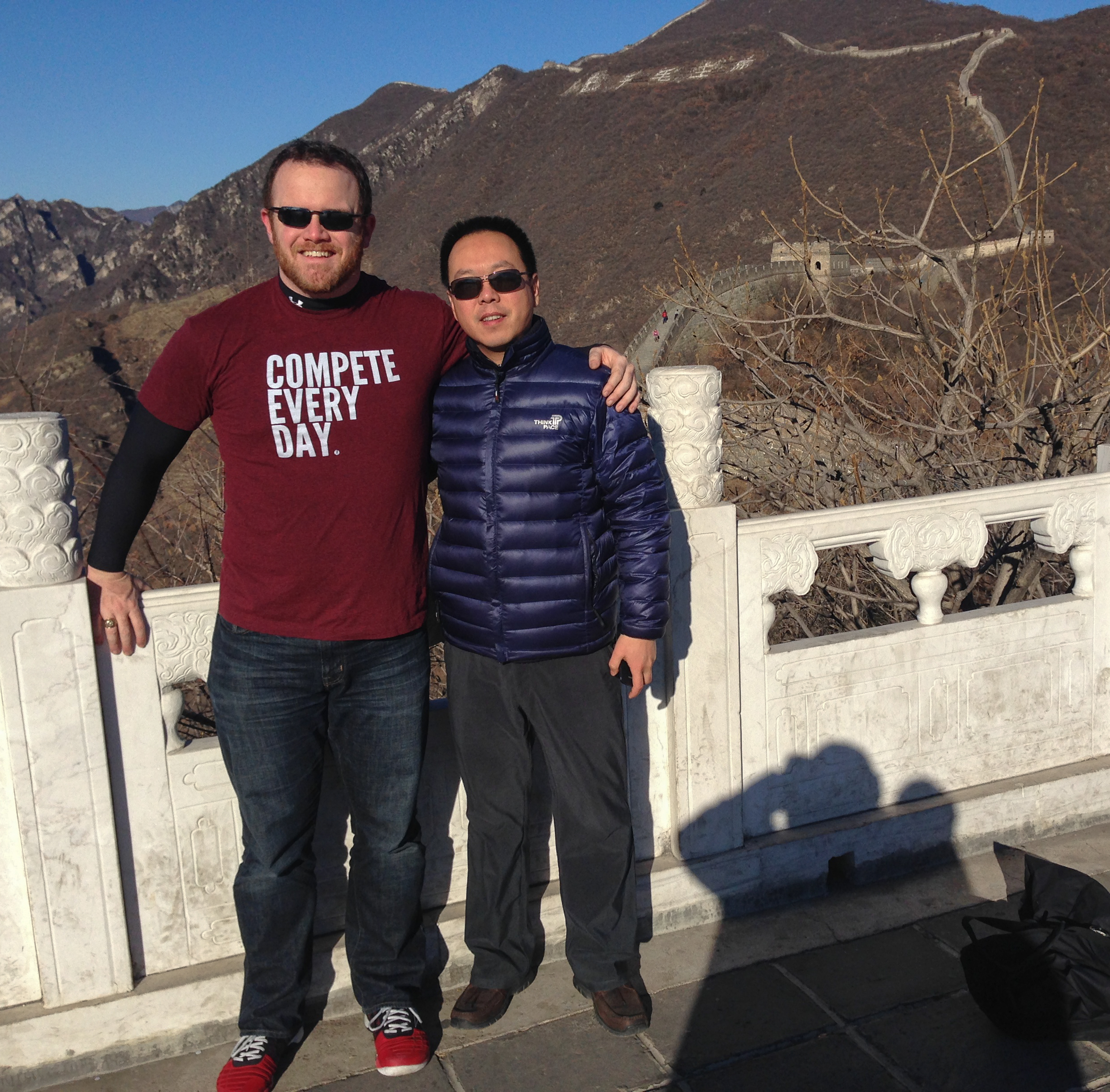 two men standing on a ledge with mountains in the background