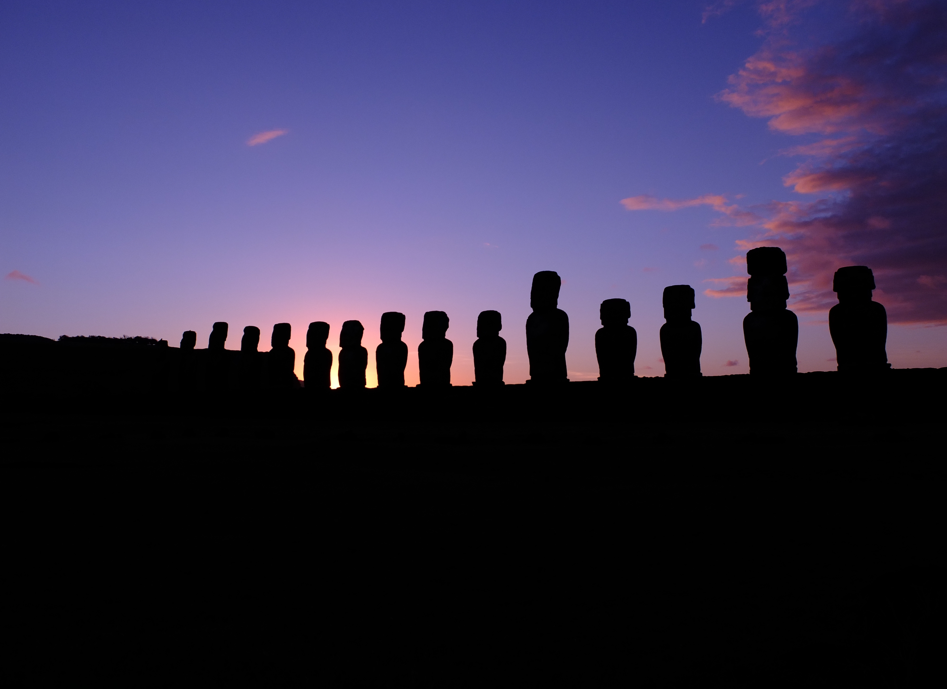 a row of statues in front of a sunset