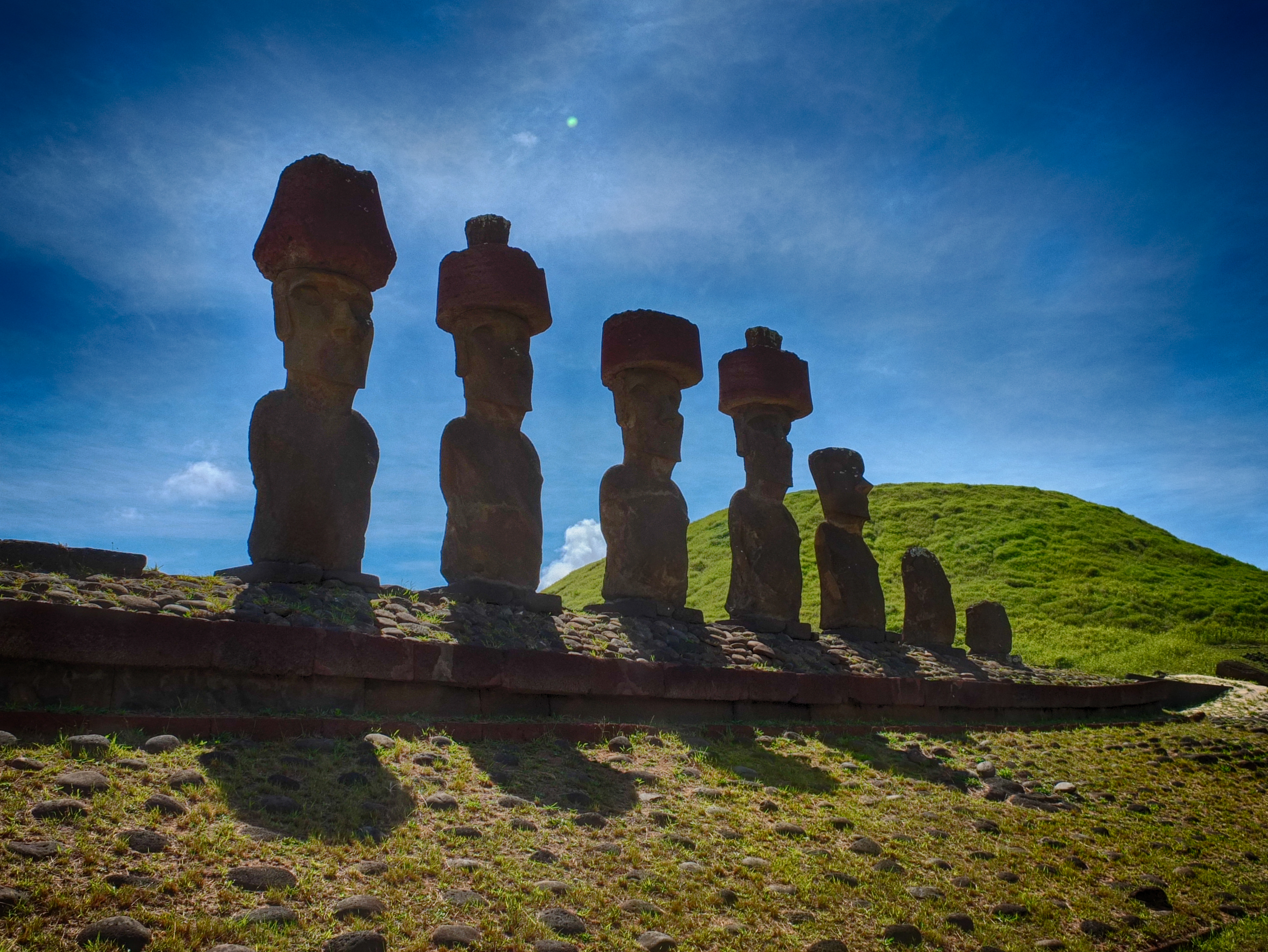a group of statues on a hill with Easter Island in the background