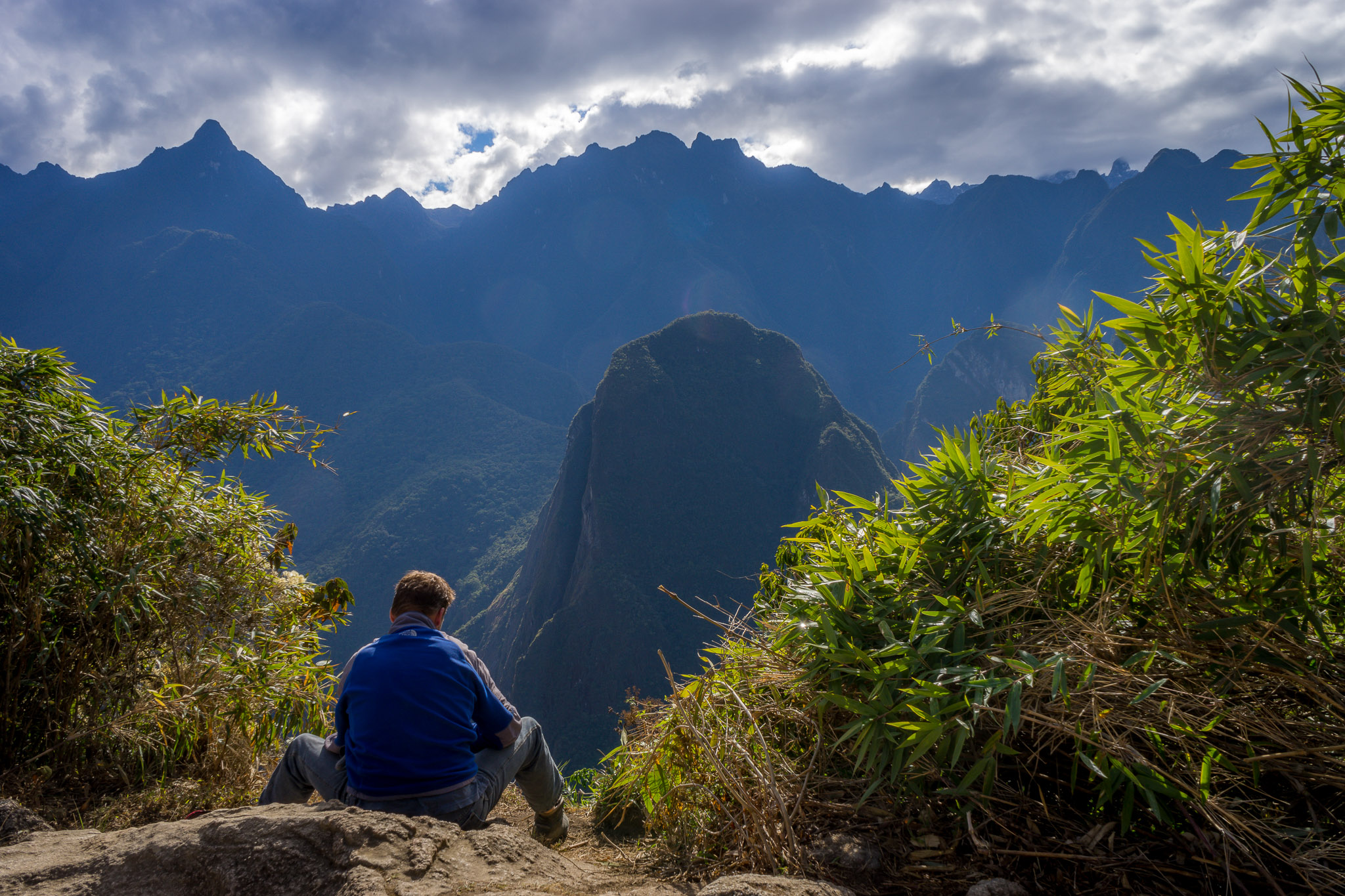 a man sitting on a rock looking at mountains