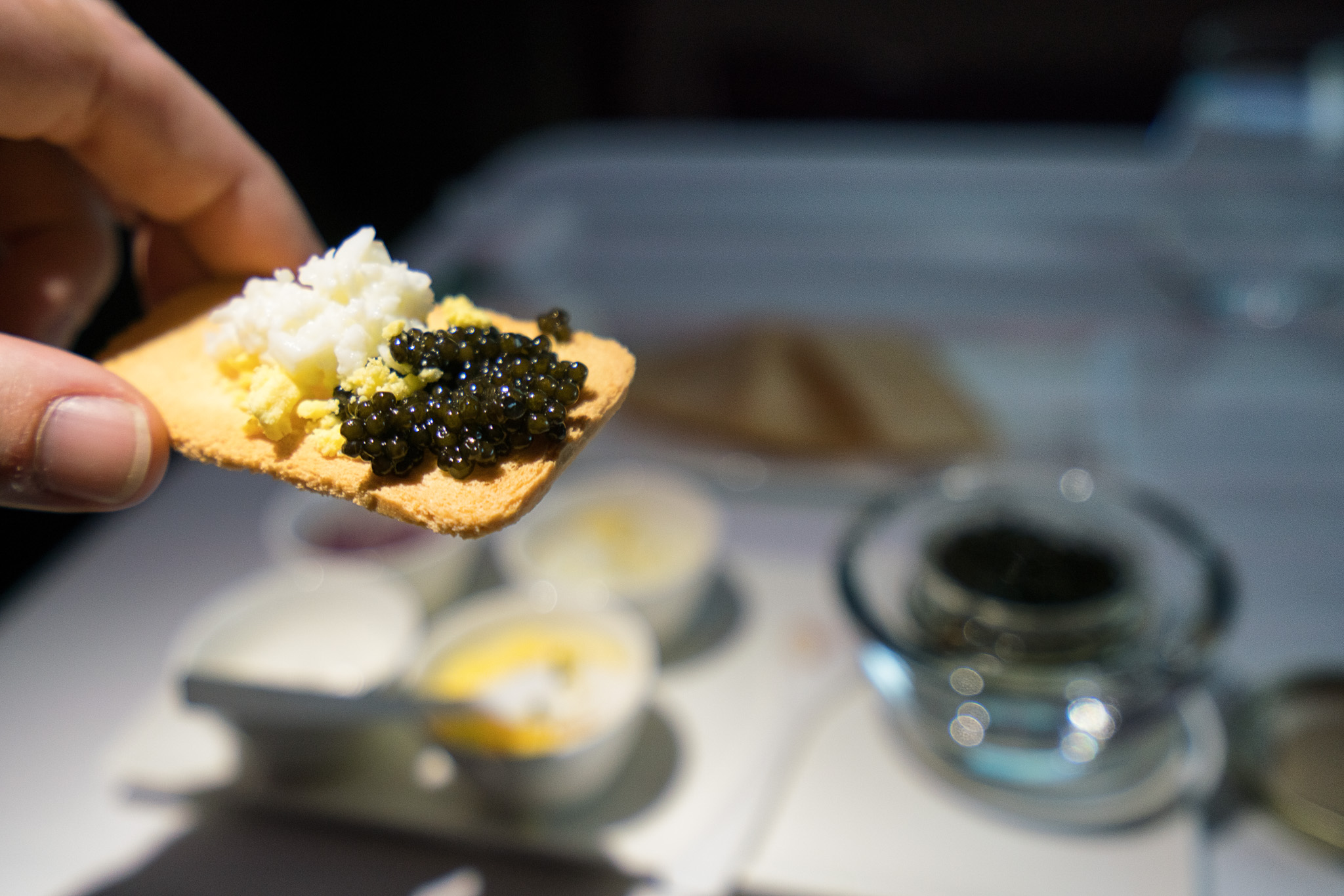 a hand holding a cracker with black and white caviar