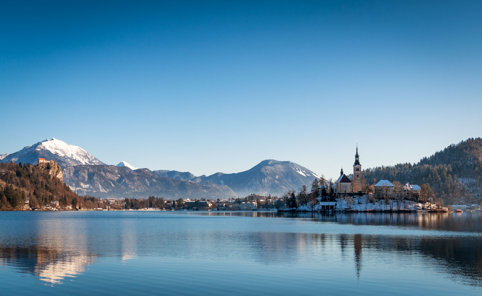 a lake with a church and mountains in the background