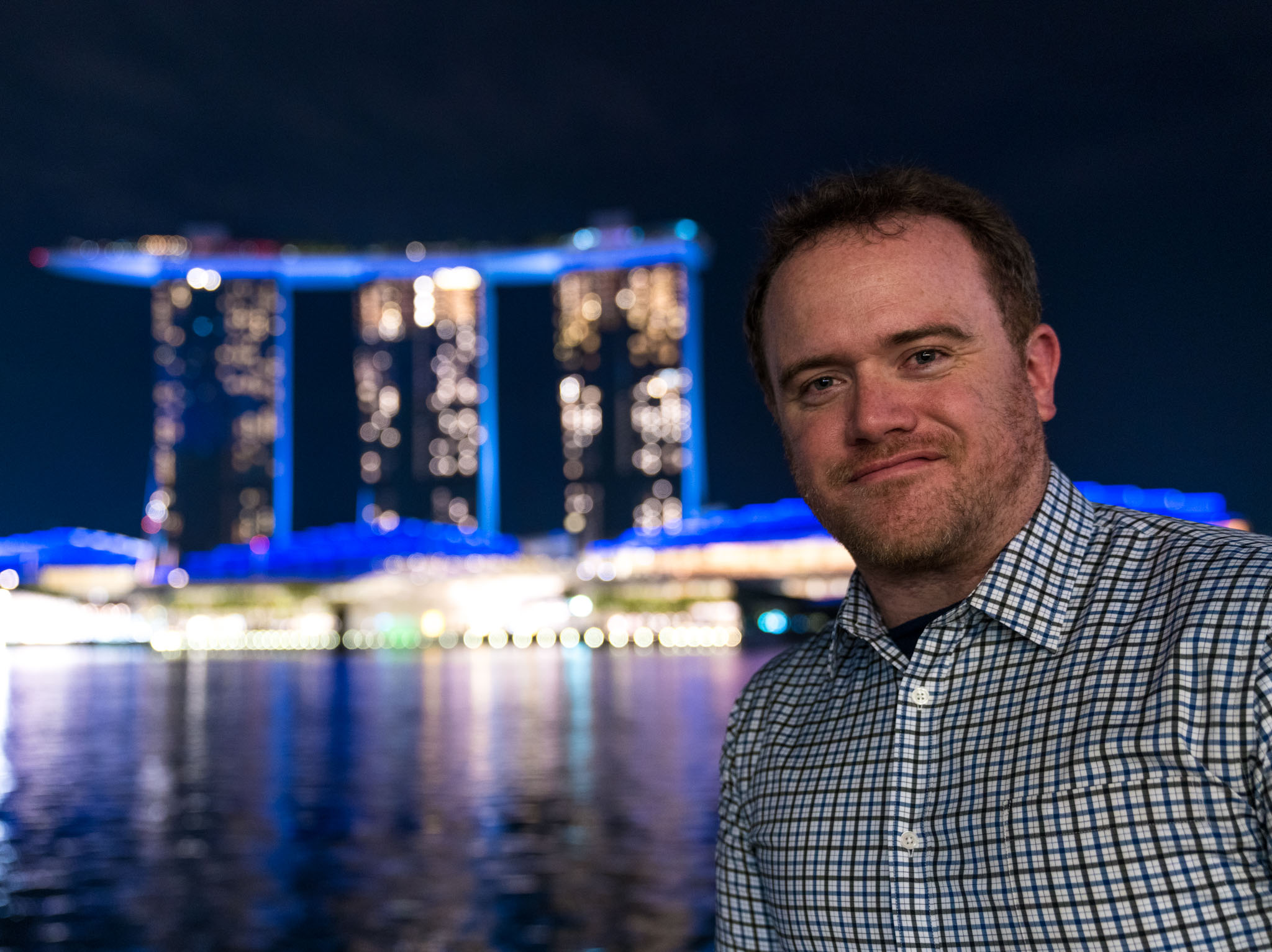 a man standing in front of a body of water with a city in the background