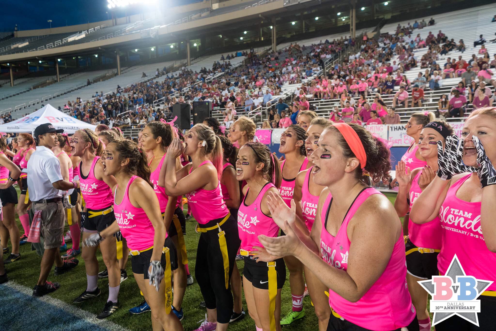 a group of women in pink shirts singing in a stadium