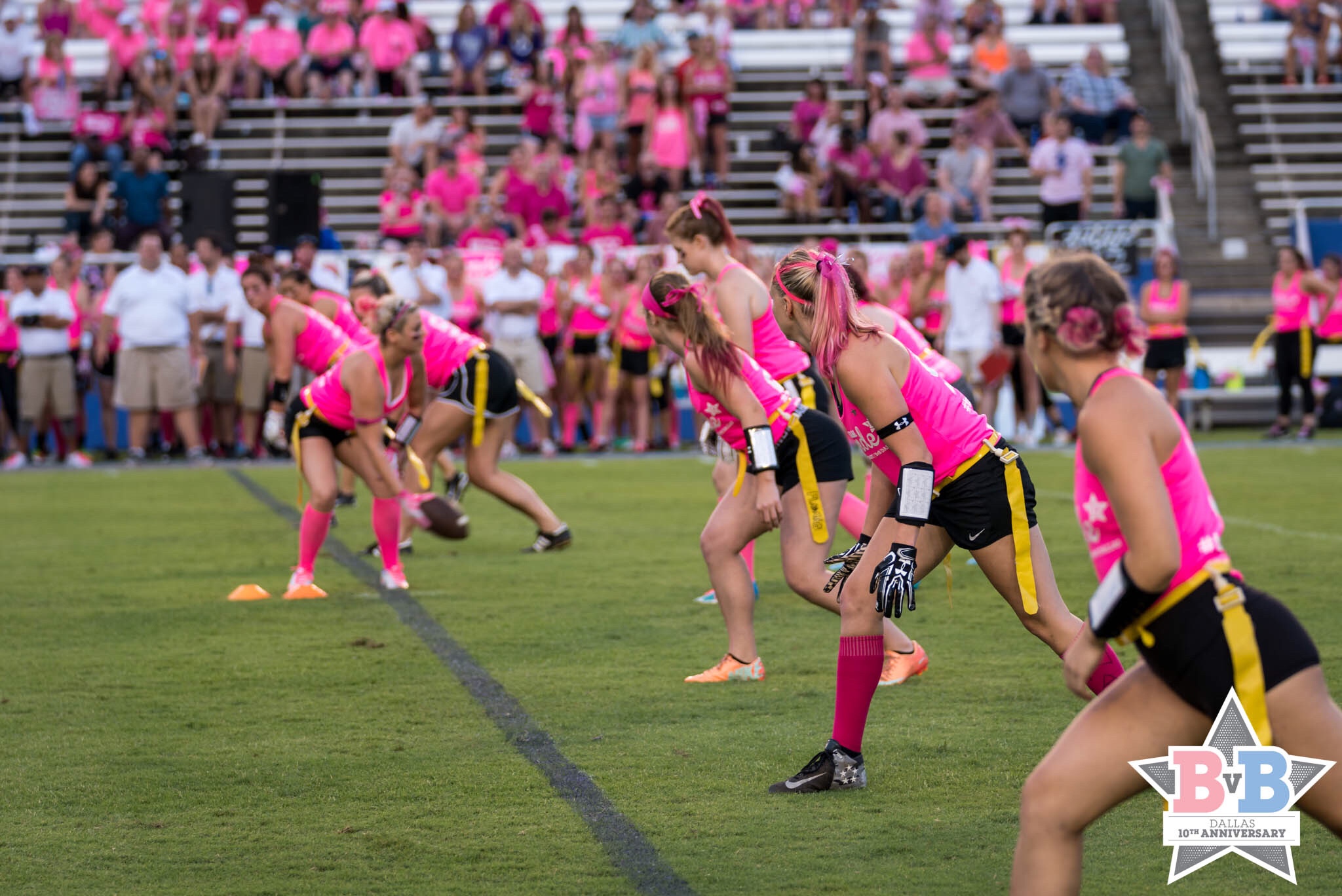 a group of women in pink shirts on a field with a crowd