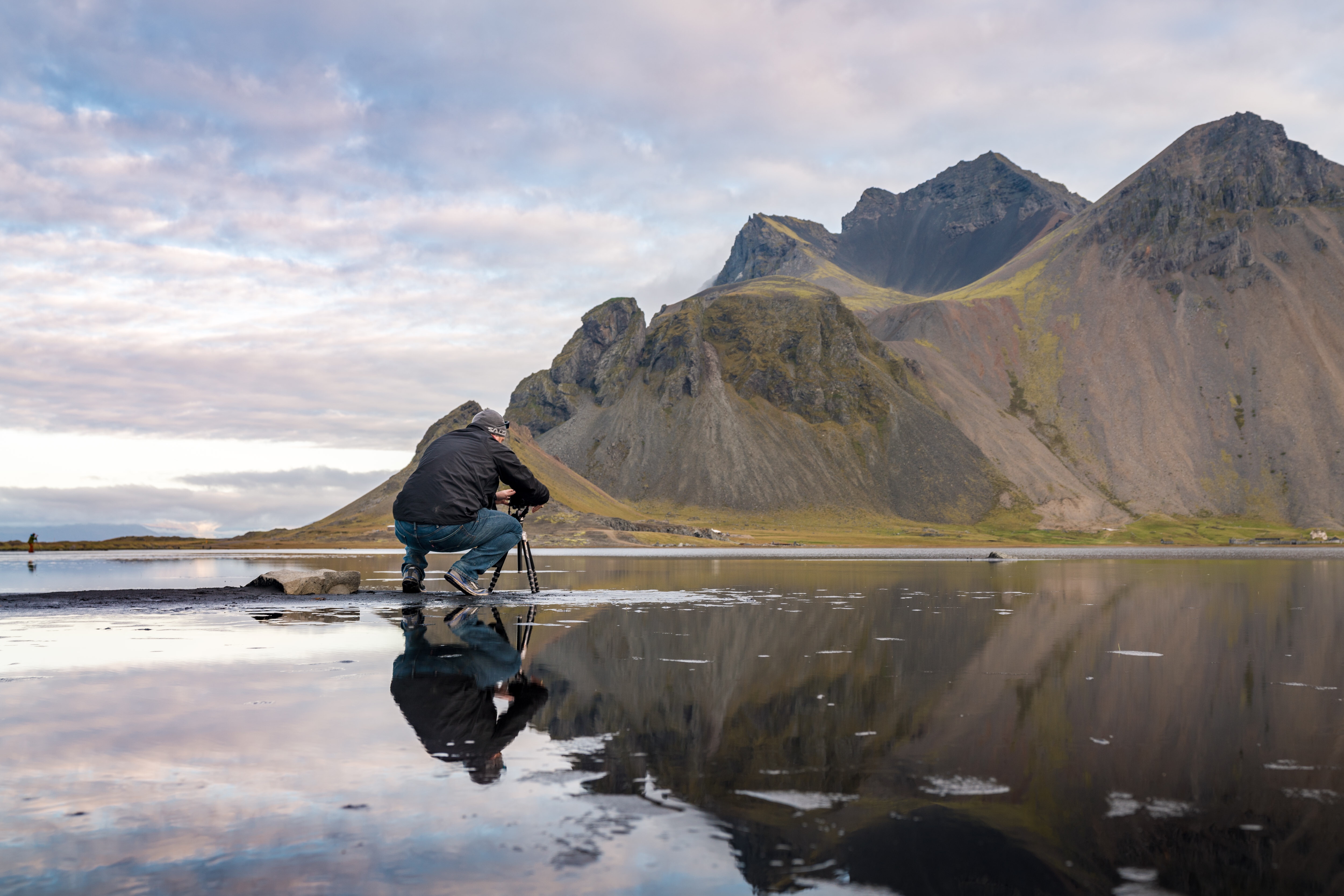 a man sitting on a mirror in a lake with mountains in the background