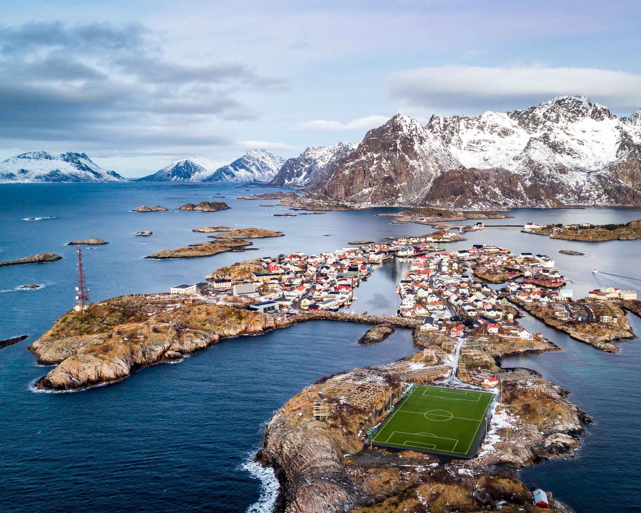 a small town on an island surrounded by water with snow covered mountains with Lofoten in the background