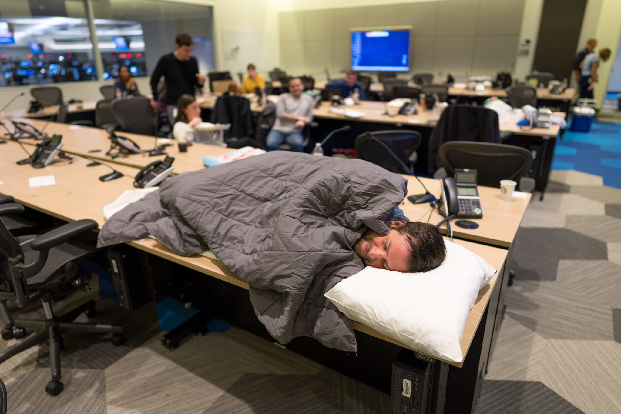 a man sleeping on a desk with a blanket