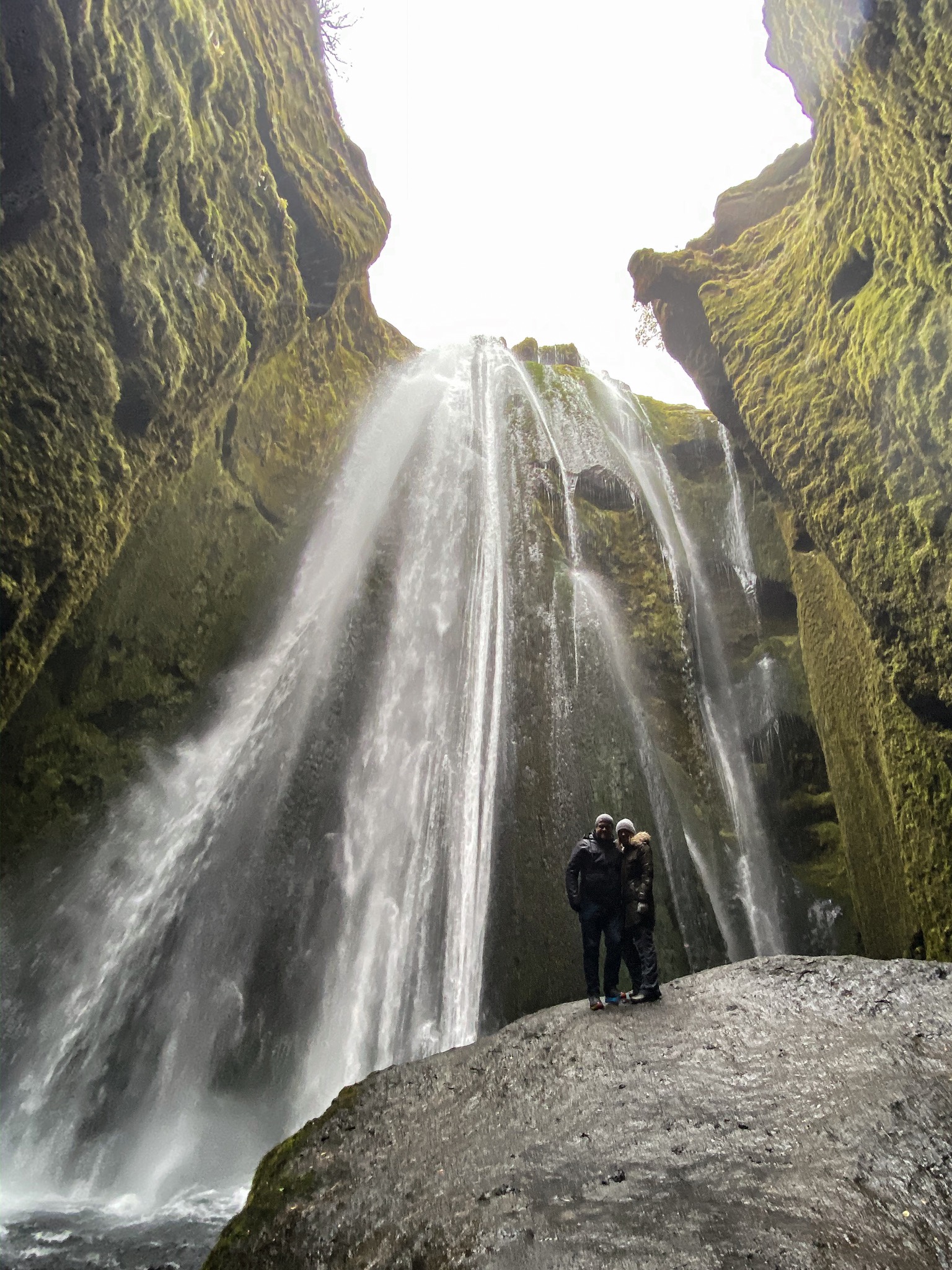 a couple of people standing on a rock with a waterfall