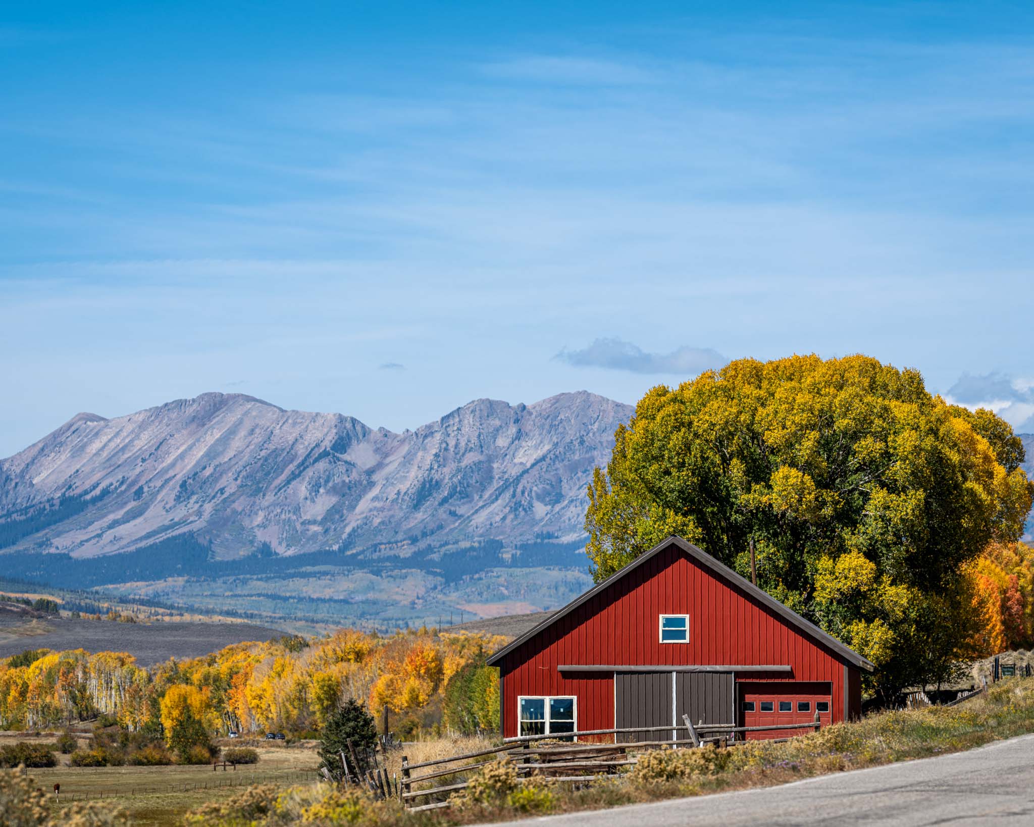 a red barn next to a road with mountains in the background